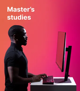 A KTU School of Economics and Business student working on a computer against a red decorative background. The faculty offers master’s studies. Choose KTU master’s studies.